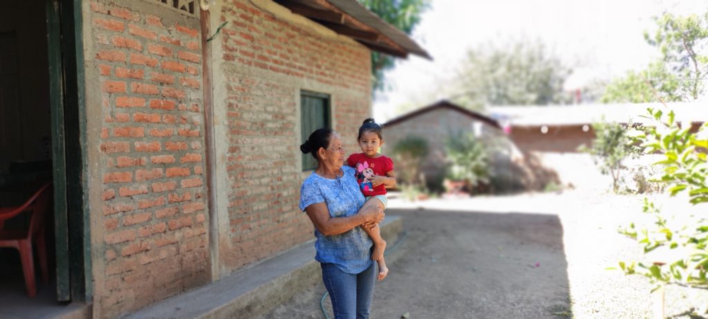 Farmer Justina Valdivia with her child in front of a brick house