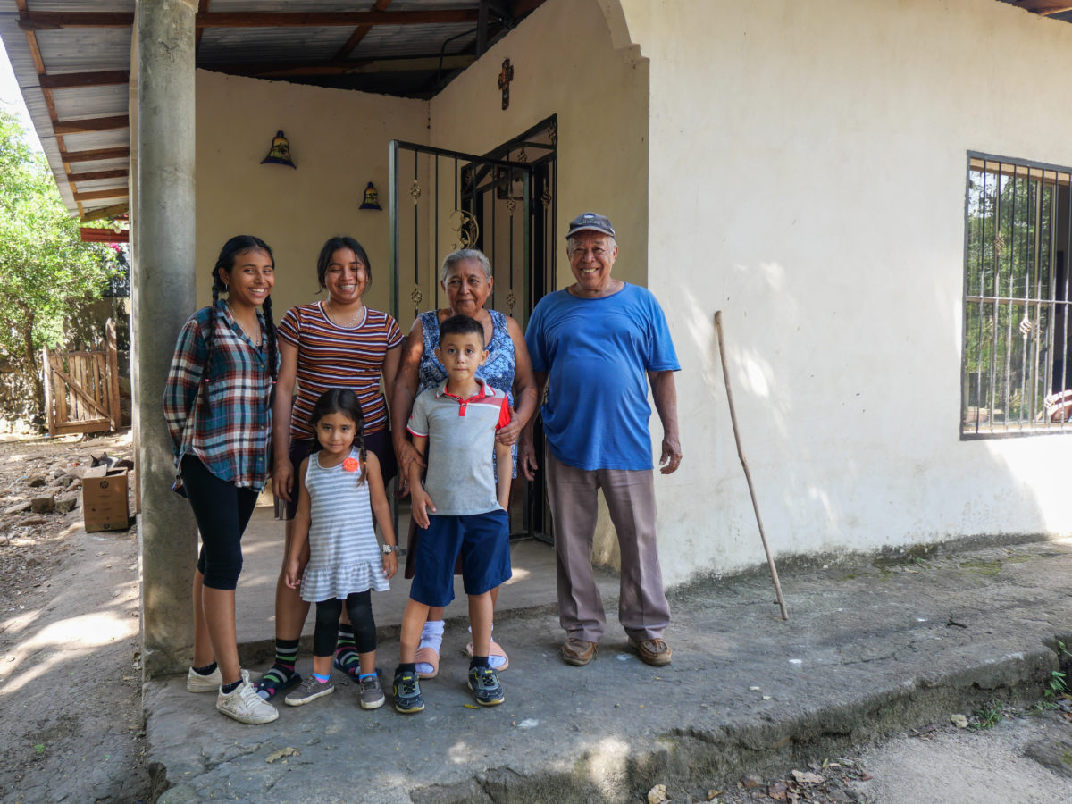 A farmer and his family smile at the camera while standing next to a building