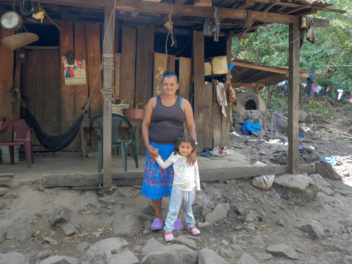A woman and her granddaughter stand outside a wooden house